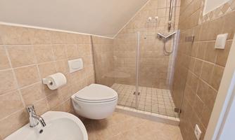 A modern bathroom with beige tiles and an open shower. It is clean and well lit, with a toilet and a bidet.