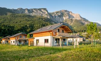 A modern house in a rural setting with mountains in the background. The green meadows and the clear sky create an idyllic atmosphere.