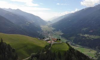 A picturesque valley landscape surrounded by mountains with green meadows and forests. In the valley lies a small village, enveloped by nature.