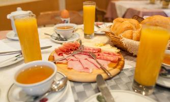 A hearty breakfast arrangement on a table. There are cold cuts, fresh rolls, orange juice, and tea.