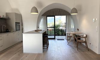 A modern apartment with an open kitchen and a dining area. Large windows provide a view of nature and plenty of daylight.