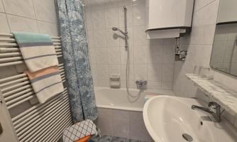 A small bathroom with a bathtub and a shower. The walls are tiled, and there are towels as well as a modern faucet.