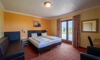 A bright hotel room with two single beds and a cozy seating area. Large windows provide a view outside and create an inviting atmosphere.