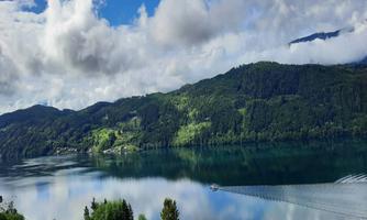 A tranquil lake surrounded by green mountains and a cloudy sky landscape. The water reflects the natural beauty of the surroundings.