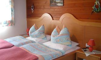 A cozy bedroom with two beds and colorful cushions. The wall is made of wood and a window lets natural light in.