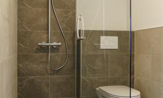 A modern bathroom with a glass shower enclosure and a wall-mounted toilet. The walls are in neutral tones.