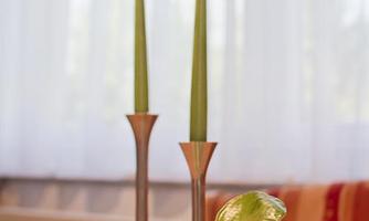 A set table with two green candles and a bowl of fresh salad. The background features large windows with a bright curtain.
