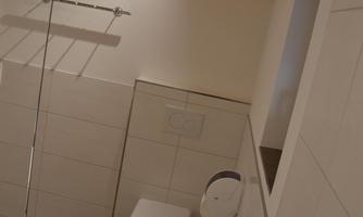 A modern bathroom with a white toilet and bright tiles. The walls are clean and the room has a cozy wooden ceiling.