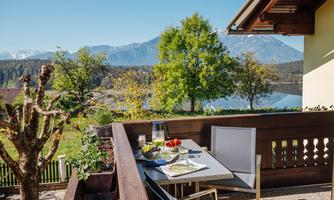 A beautiful balcony with a table set for breakfast. In the background, mountains and a calm lake can be seen.