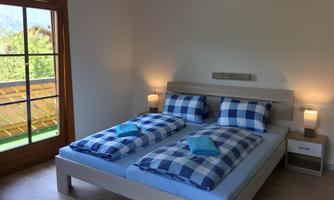 A bright bedroom with two beds and checked bedspreads. Next to the bed are nightstands with lamps and a view of a balcony.