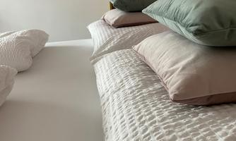 A cozy bed with several pillows in soft colors. In the background, decorative wall art and a lamp can be seen.