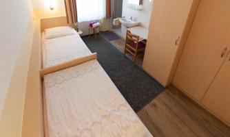 A simple room with two single beds and a large window. There is a wardrobe and a small seating area.
