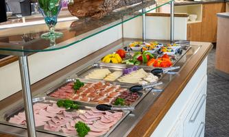 A lavish buffet featuring a selection of cold cuts, cheese, and fresh fruit. A blooming plant element adds an attractive touch to the presentation.