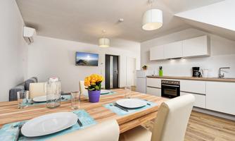 A modern kitchen with a wooden dining table and four chairs. On the table, there is a pot with yellow flowers and the table is set with dishes.