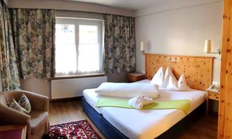 A cozy hotel room with a double bed and wooden paneling. The room has light curtains and offers a pleasant atmosphere.