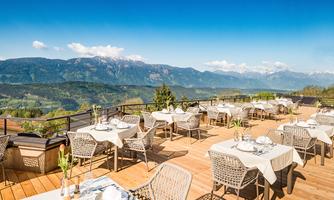 A beautiful terrace with tables and chairs, offering a view of the mountains. The sky is clear and blue, perfect for an outdoor meal.