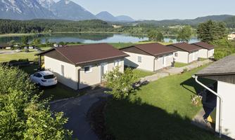 A quiet landscape with several vacation homes by the water. In the background, there are mountains and a clear sky.