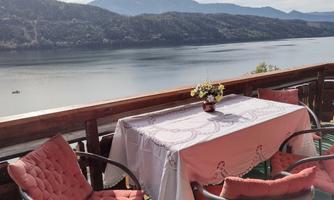 A beautiful view of a calm lake with a cozy terrace.  
On the table, there is a flower vase, and the surroundings are surrounded by gentle hills.
