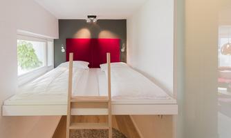 A modern room with a loft bed and two beds. The wall is designed in elegant colors and there is plenty of daylight.