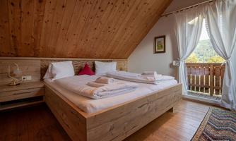 A cozy bedroom with a large wooden bed and white bed linens. Through the window, you can see a beautiful view of nature.