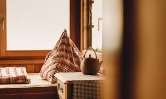 A cozy room with a wooden window and a cushioned area. A teapot and a checkered pillow are on the table.