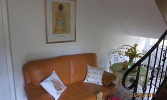 A cozy living room with an orange couch and decorative cushions. Next to the couch is a glass table with flowers and a small toy bear.
