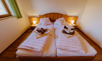 A cozy bedroom with two single beds and soft blankets. The wooden details and gentle lighting create an inviting atmosphere.