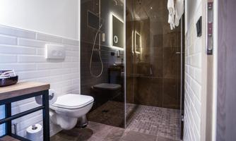 A modern bathroom with a shower and a toilet. The walls are partially tiled, and there is a wooden base with a towel holder.