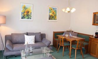 A cozy living room with a gray sofa and a wooden table. Pictures of sunflowers hang on the walls.