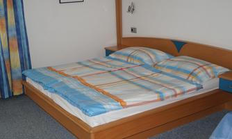A simple bedroom with a large bed and striped bedspreads. On the wall, there is a picture and curtains in bright colors.