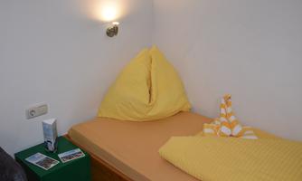 A simple room with a bed and yellow cushions. Next to the bed are small objects and a lamp on the wall.