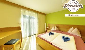 A bright room with two single beds, a table, and a chair. The walls are painted in soft colors, and large windows provide plenty of daylight.