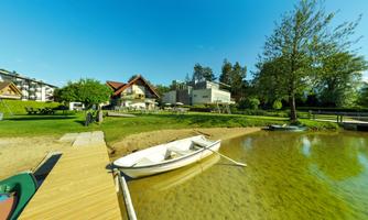 A peaceful landscape with a boat by the shore. In the background, you can see a house and trees under a clear blue sky.