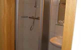 A small bathroom area with a shower cubicle and a sink. The walls are tiled and there is a waste bin on the floor.
