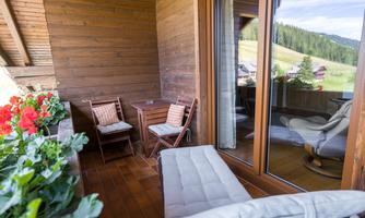 A cozy balcony with wooden paneling and beautiful flowers. Two chairs and a table invite you to relax.