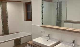 A modern bathroom with two sinks and a large mirror. The walls are plain and well-lit, featuring an elegant bathtub and ample storage space.