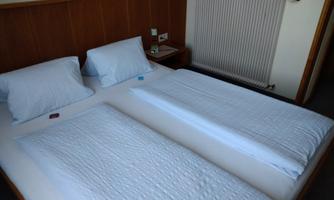 A simple bedroom with two single beds and white bed covers. There is a radiator on the wall and a nightstand.