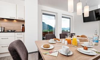 A modern dining room with a table set for breakfast. In the background, there are windows overlooking a picturesque landscape.