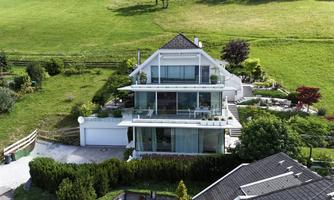 A modern house with large windows and a beautiful garden.  
It is situated in a green, hilly landscape.