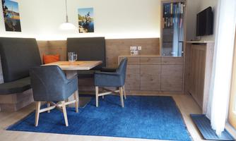 A modern dining room with a table and comfortable chairs. The walls are decorated with pictures, and there is a television as well as cozy lighting.