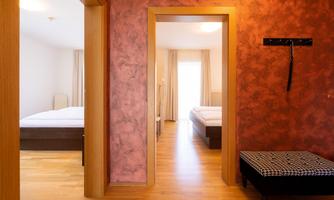 A bright hallway with two rooms connected by an open door. The floor is wooden and the walls are designed in warm colors.