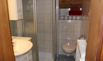 A small bathroom with a shower, sink, and toilet. The walls are tiled and there are wooden details.