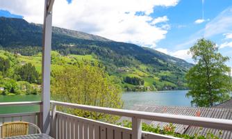 A picturesque view of a lake, surrounded by green hills and mountains. The sky is clear with some clouds, and nature radiates tranquility.