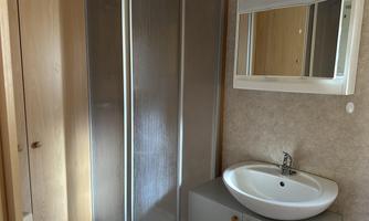 A modern bathroom with a shower and a sink. The walls are light-colored and the fittings are kept simple.