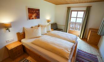 A cozy bedroom with a double bed and white bedcovers. It has wooden paneling and a large window with a view outside.