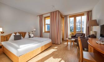 A bright and cozy hotel room with a double bed and large windows. The room contains a table, a chair, and a television.