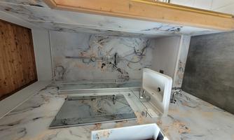 A modern bathroom with a shower and a sink. The walls are decorated with a marbled pattern and the floor is gray.