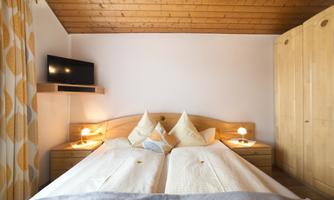 A cozy bedroom with two beds and wooden ceilings. The room has a warm atmosphere and is equipped with a television.