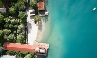 A beautiful beach with gentle water and a small sunbathing area. In the background, trees and a building can be seen.