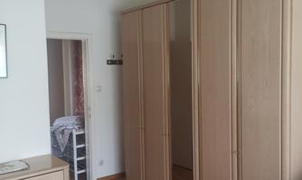 A simple room with a large wardrobe and a wooden floor. An elegant light hangs from the ceiling.